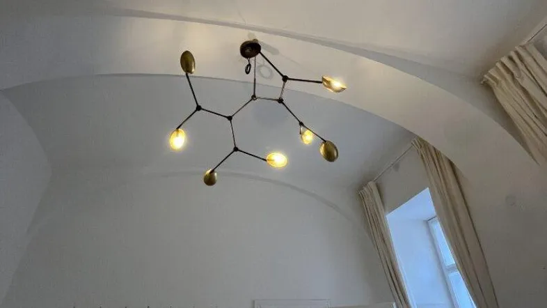 Geräumiger Innenraum mit hohen Gewölbedecken, einem modernen Kronleuchter und einem Fenster mit Vorhängen.