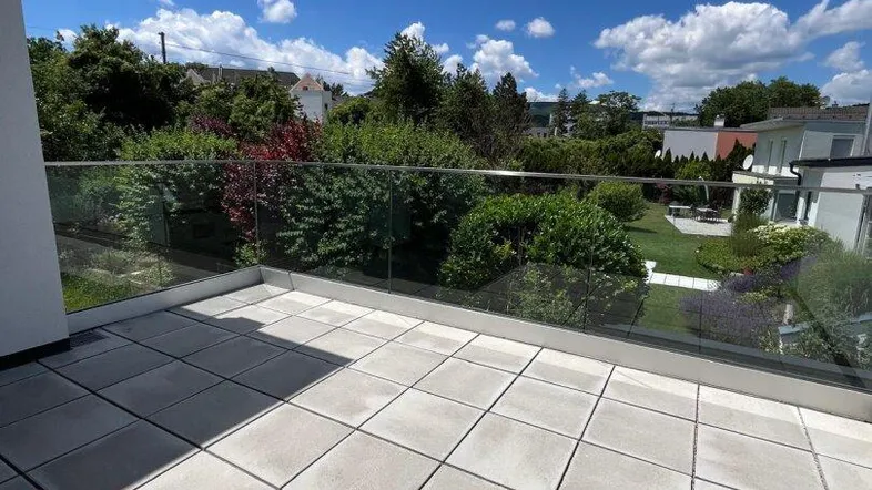 Geräumiger Balkon mit Fliesenboden und Glasgeländer, bietet einen schönen Ausblick.