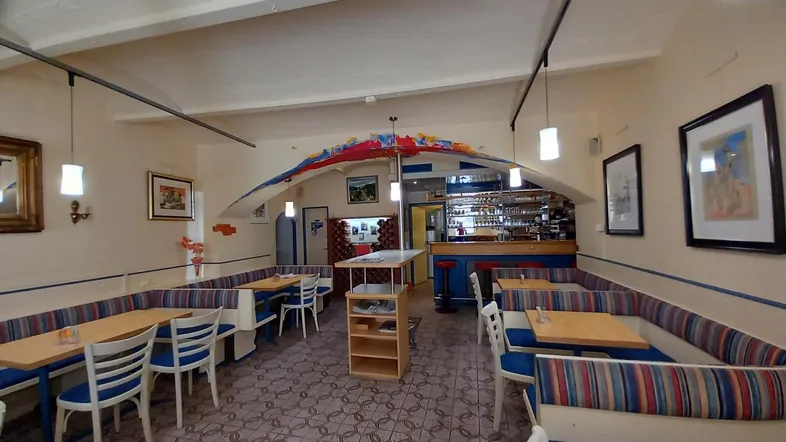 Geräumiger Gastraum mit Sitzbänken, Tischen und einer Bar im Hintergrund, ideal für gesellige Runden.