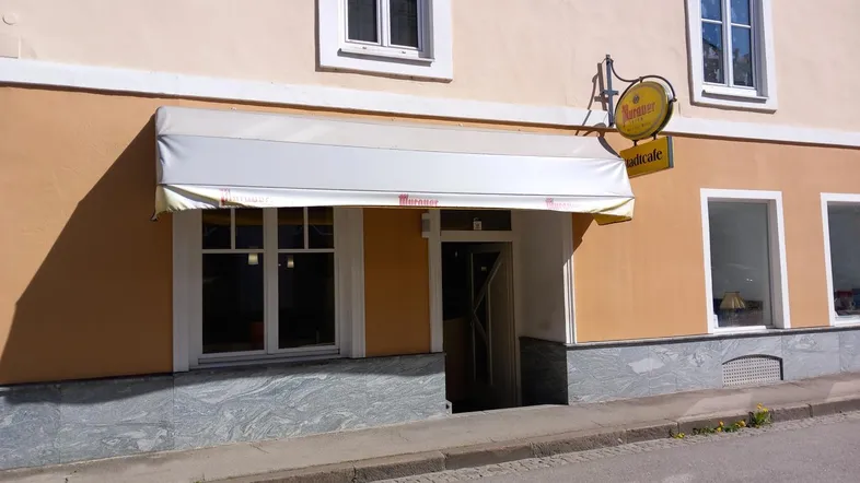 Fassade eines Gebäudes mit einem Café-Eingang, Markise und Fenstern zur Straße hin.