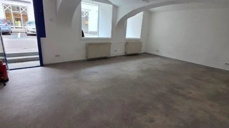 Geräumiger Gewerberaum mit gewölbter Decke, Betonboden und Blick auf die Straße durch die offene Tür.