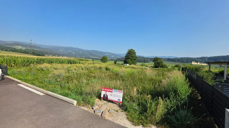 Ungenutztes Grundstück mit Verkaufsanzeige, umgeben von Feldern und ländlicher Landschaft.