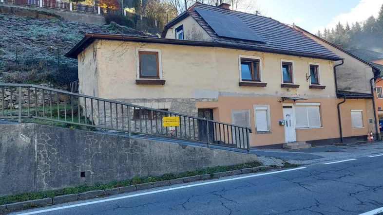Ansicht eines Hauses an einem Hang mit Solarpaneelen auf dem Dach und einer Straße im Vordergrund.