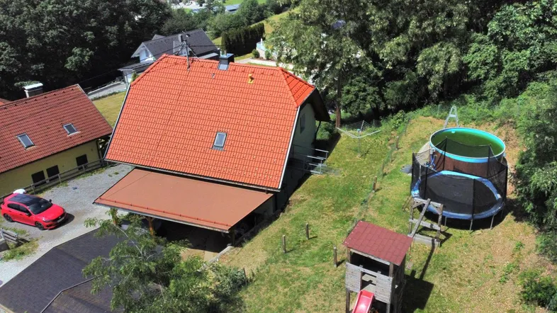 Luftaufnahme eines Hauses mit rotem Dach, Garten, Aufstellpool, Trampolin und Spielplatz.