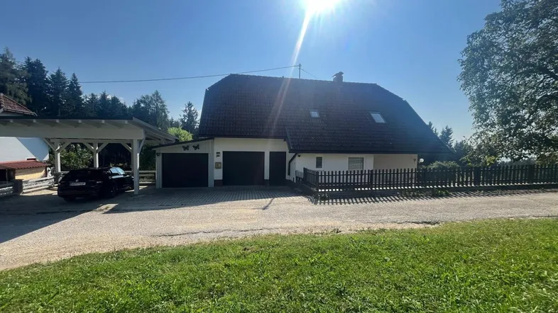 Einfamilienhaus mit Satteldach, Carport und großem Vorgarten unter strahlendem Sonnenschein.