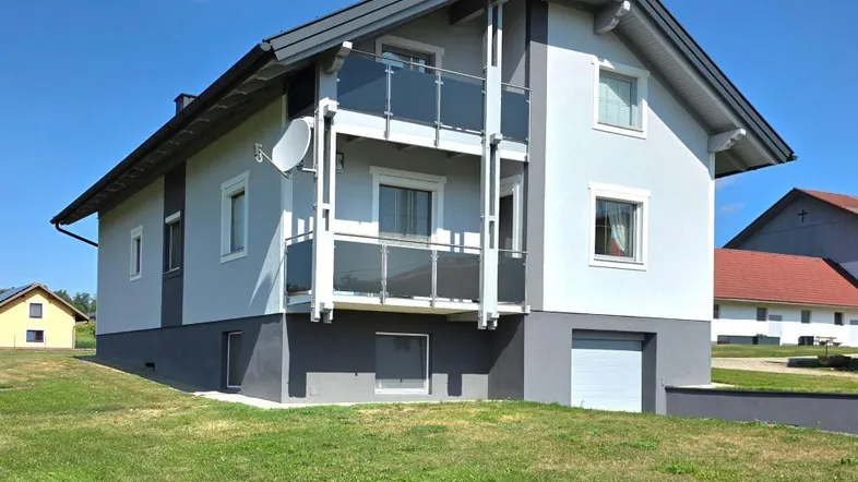 Modernes Einfamilienhaus mit zwei Balkonen und integrierter Garage, umgeben von einer grünen Wiese.