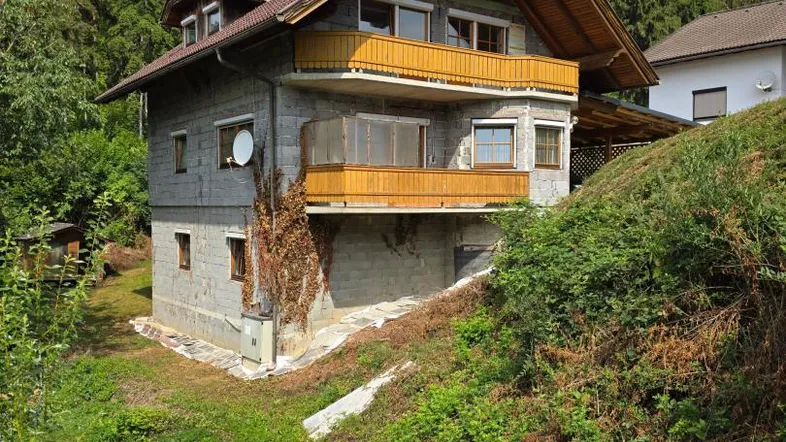 Haus in Hanglage mit Wald im Hintergrund und unfertiger Fassade, bietet Potenzial zur Gestaltung.