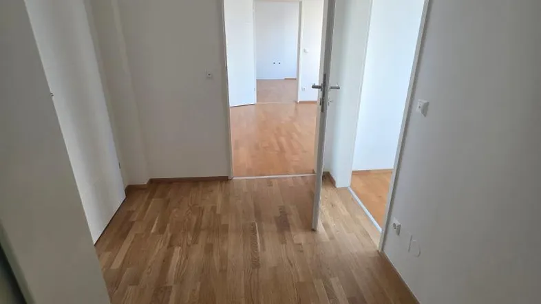 Heller Flur mit Holzboden und weißen Wänden, der zu weiteren Zimmern führt.