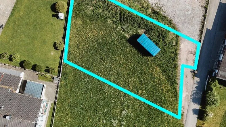 Luftaufnahme eines Grundstücks mit blauer Umrandung, umgeben von Häusern und Grünflächen.
