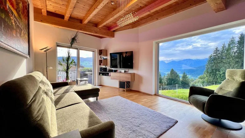 Helles Wohnzimmer mit Holzbalkendecke, großen Panoramafenstern und beeindruckendem Bergblick.