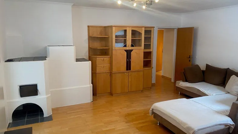 Geräumiges Wohnzimmer mit hellem Parkettboden, gemütlichem Kaminofen und bequemer Sofalandschaft.