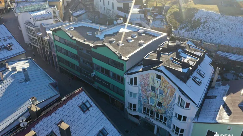 Luftaufnahme der Stadtansicht mit verschiedenen Gebäuden, darunter ein markantes grünes Gebäude und schneebedeckte Dächer.