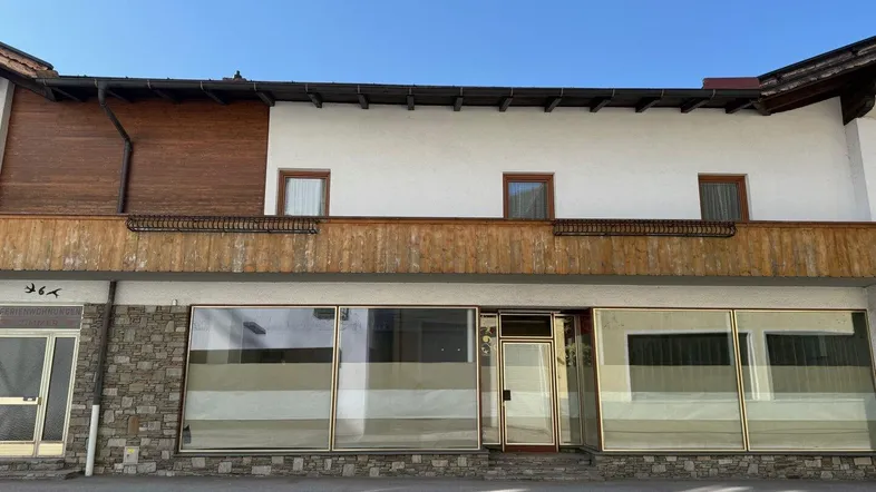 Fassade eines Gebäudes mit großen Schaufenstern im Erdgeschoss und traditionellen Holzelementen im Obergeschoss.