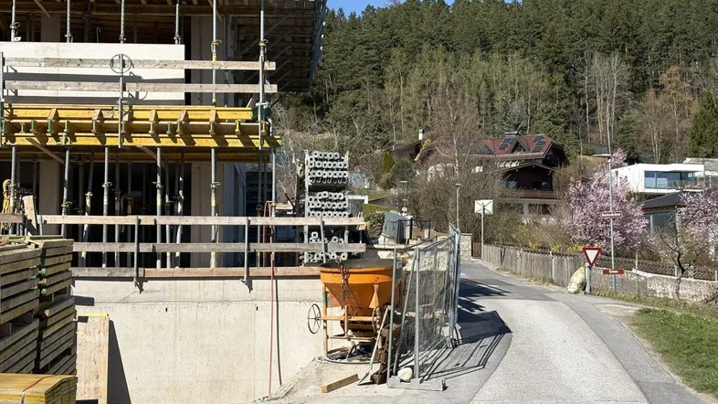 Neubau im Rohbauzustand mit Gerüst und Blick auf bewaldete Hügel und eine Landstraße.