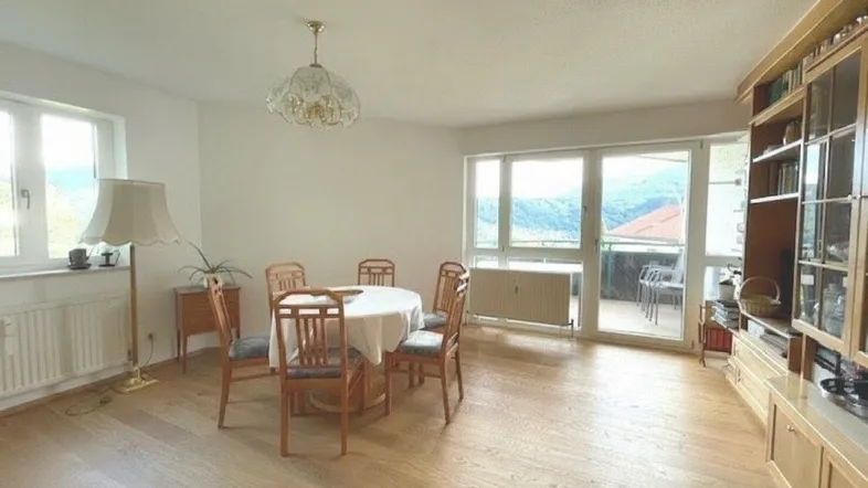 Heller Wohn- und Essbereich mit Holzboden und Zugang zum Balkon mit Bergblick.