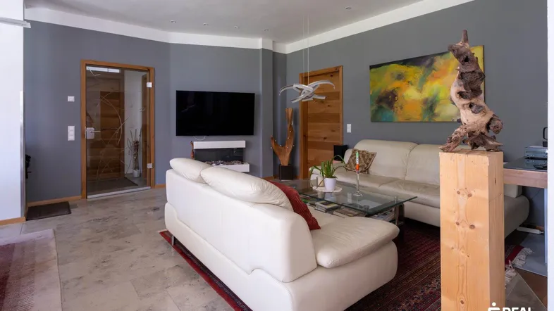 Geräumiges Wohnzimmer mit beigen Ledersofas, Steinfliesenboden und moderner Kunst an der grauen Wand.