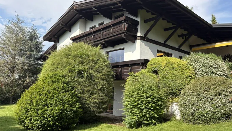 Traditionelles Haus im alpenländischen Stil mit gepflegtem Garten und üppiger Bepflanzung unter blauem Himmel.