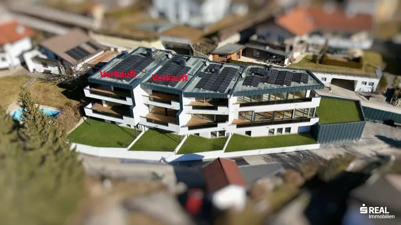 Luftaufnahme eines modernen Wohnkomplexes mit Photovoltaikanlagen auf den Dächern und umliegender Bebauung.