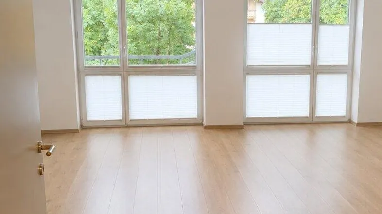 Heller Wohnraum mit großen Giebelfenstern, Holzbalken und modernem Laminatboden.