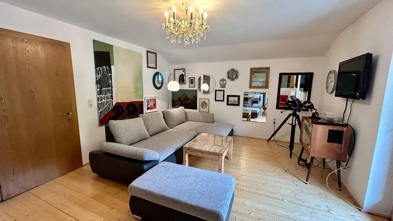 Helles Wohnzimmer mit großem Ecksofa, Holzboden und einem Kronleuchter an der Decke.