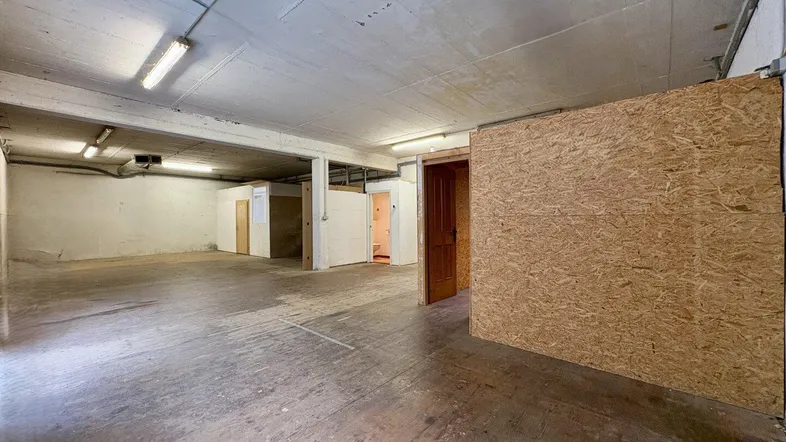 Großer Kellerraum mit Betonboden und -decke, ausgestattet mit Leuchtstoffröhren und einfachen Trennwänden.