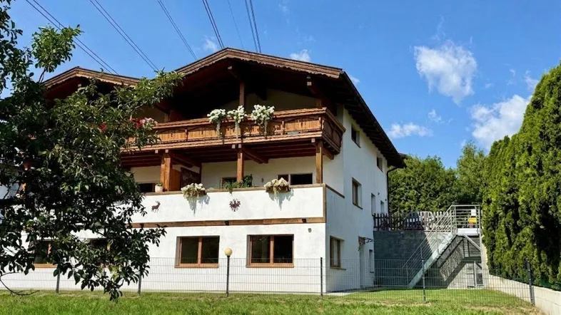 Traditionelles Haus mit Holzbalkonen und grüner Umgebung unter blauem Himmel.