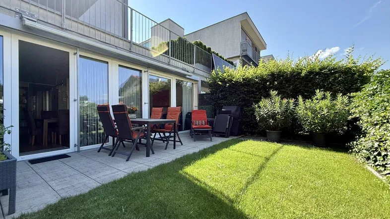 Sonniger Außenbereich mit gepflasterter Terrasse, Rasenfläche und Gartenmöbeln, ideal zum Entspannen.
