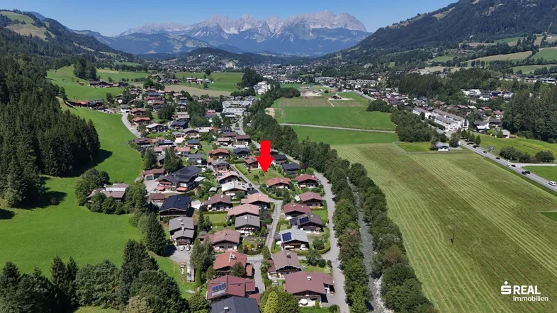 Luftaufnahme eines Dorfes in einem Tal mit majestätischen Bergen im Hintergrund, das Grundstück ist markiert.