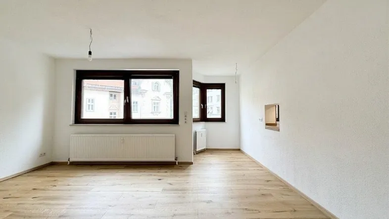 Helles Zimmer mit neuem Holzboden und großen Fenstern, bereit für die individuelle Gestaltung.