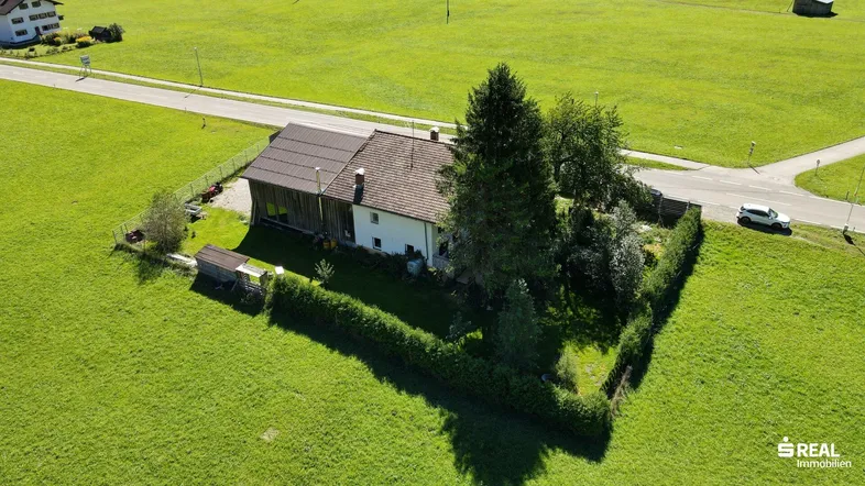 Luftaufnahme eines Hauses umgeben von grünen Wiesen mit angrenzender Straße und ländlicher Umgebung.