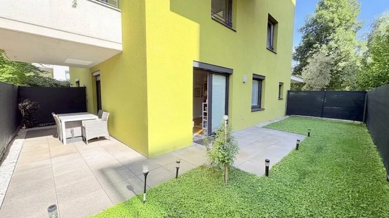 Moderne gelbe Fassade mit einer möblierten Terrasse und einem kleinen Rasenbereich.