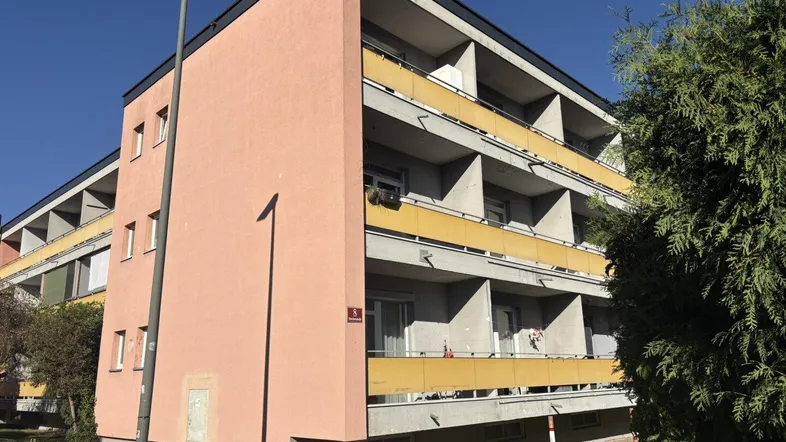 Mehrfamilienhaus mit rosafarbener Fassade und gelben Balkonen unter blauem Himmel.