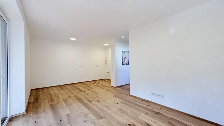Helles, leeres Zimmer mit neuem Holzboden und Zugang zu einem Balkon.