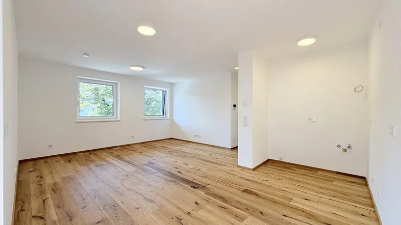 Helles, leeres Zimmer mit breiten Holzplanken und modernen Deckenleuchten.