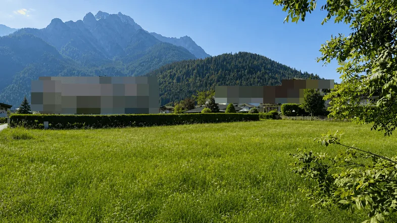 Weitläufige grüne Wiese mit majestätischem Bergblick und einer gepflegten Hecke im Vordergrund.
