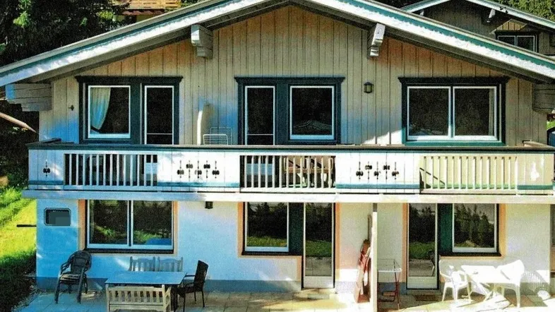 Traditionelles Chalet mit Balkon und Terrasse, umgeben von grünen Bäumen und Natur.