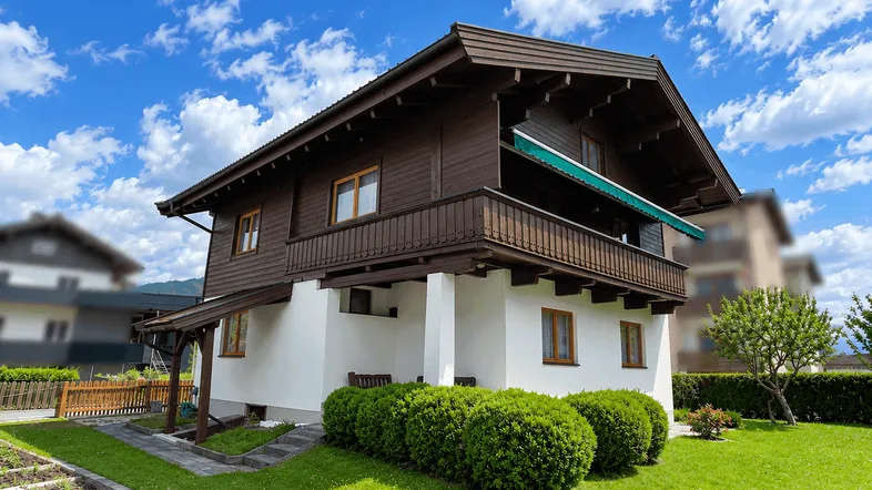 Charmantes Haus im alpinen Stil mit gepflegtem Garten und kleinem Gemüsegarten unter blauem Himmel.