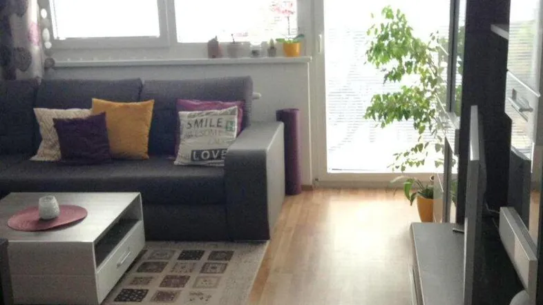 Helles Wohnzimmer mit Sofa, Couchtisch und Zugang zu einem Balkon oder einer Terrasse.