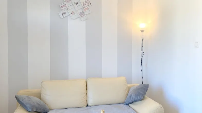 Gemütliches Wohnzimmer mit beigem Sofa, Stehlampe und gestreifter Akzentwand.