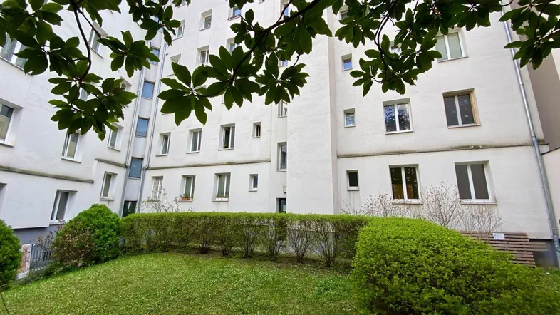Grüner Innenhof mit gepflegtem Rasen und Hecken, umgeben von der weißen Wohnhausfassade.