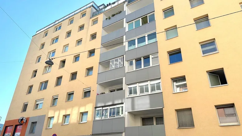 Mehrstöckiges Wohngebäude mit gelber und grauer Fassade sowie mehreren Balkonen.