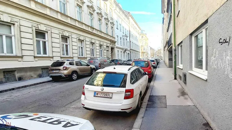Belebte Straße mit parkenden Autos und historischen Fassaden in der Stadt.
