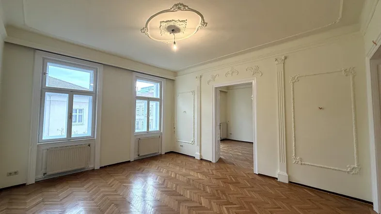 Helles Wohnzimmer mit Fischgrätparkett, Stuckdecken und dekorativen Wandelementen in einem Altbau.