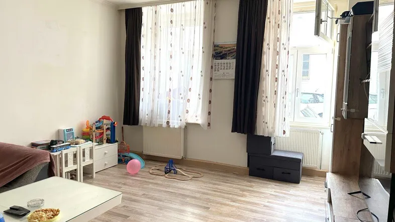 Helles Wohnzimmer mit Laminatboden, großen Fenstern und Kinderspielzeug.