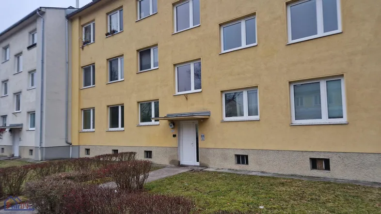 Gelbes Mehrfamilienhaus mit weißer Eingangstür und einem kleinen Vorgartenbereich.