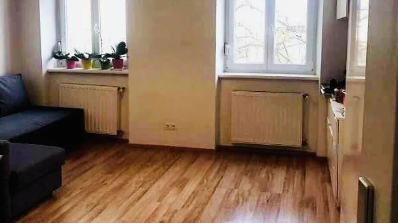 Heller Wohnbereich mit Holzboden und großen Fenstern, die viel Tageslicht hereinlassen.