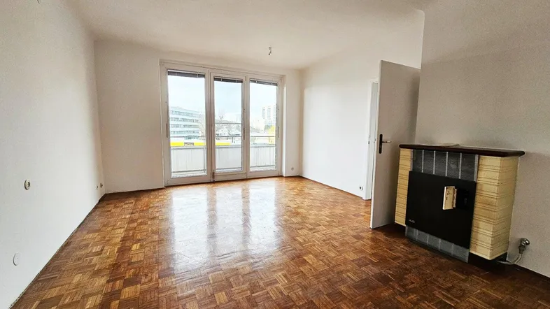 Helles Wohnzimmer mit Parkettboden, Balkonzugang und einem traditionellen Kaminofen.