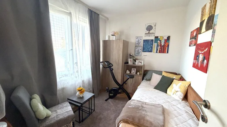 Gemütliches Schlafzimmer mit Einzelbett, Kleiderschrank und einem Fenster, das Tageslicht hereinlässt.