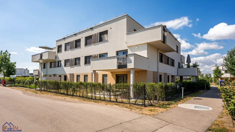 Modernes Mehrfamilienhaus mit heller Fassade, Balkonen und gepflegter Hecke im Außenbereich.
