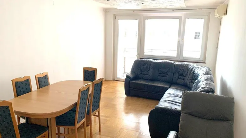 Helles Wohn- und Esszimmer mit Parkettboden, Ledersofa und Zugang zum Balkon.